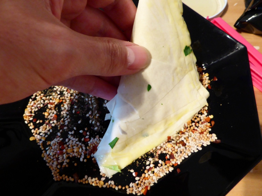 Dipping the triangle in the seed mix for the leek bourekas recipe.