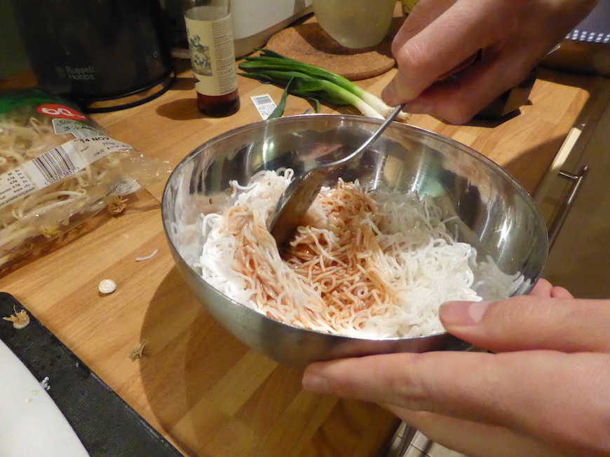 Mixing the rice noodles and the pad thai sauce in a mixing bowl